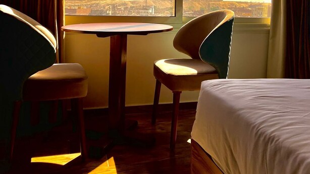 Habitación de hotel con cama, dos sillas, una mesita y un ventanal con vistas a las pirámides.