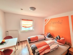A room with two beds, a window with blinds, a radiator, a small table with a flower, and a wall with a motivational quote. - Apartment '70m²' with Shared Garden, Balcony and Wi-Fi (Hayingen)