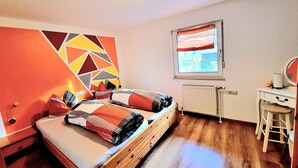 Un dormitorio con cama, escritorio, radiador y ventana con cortinas.