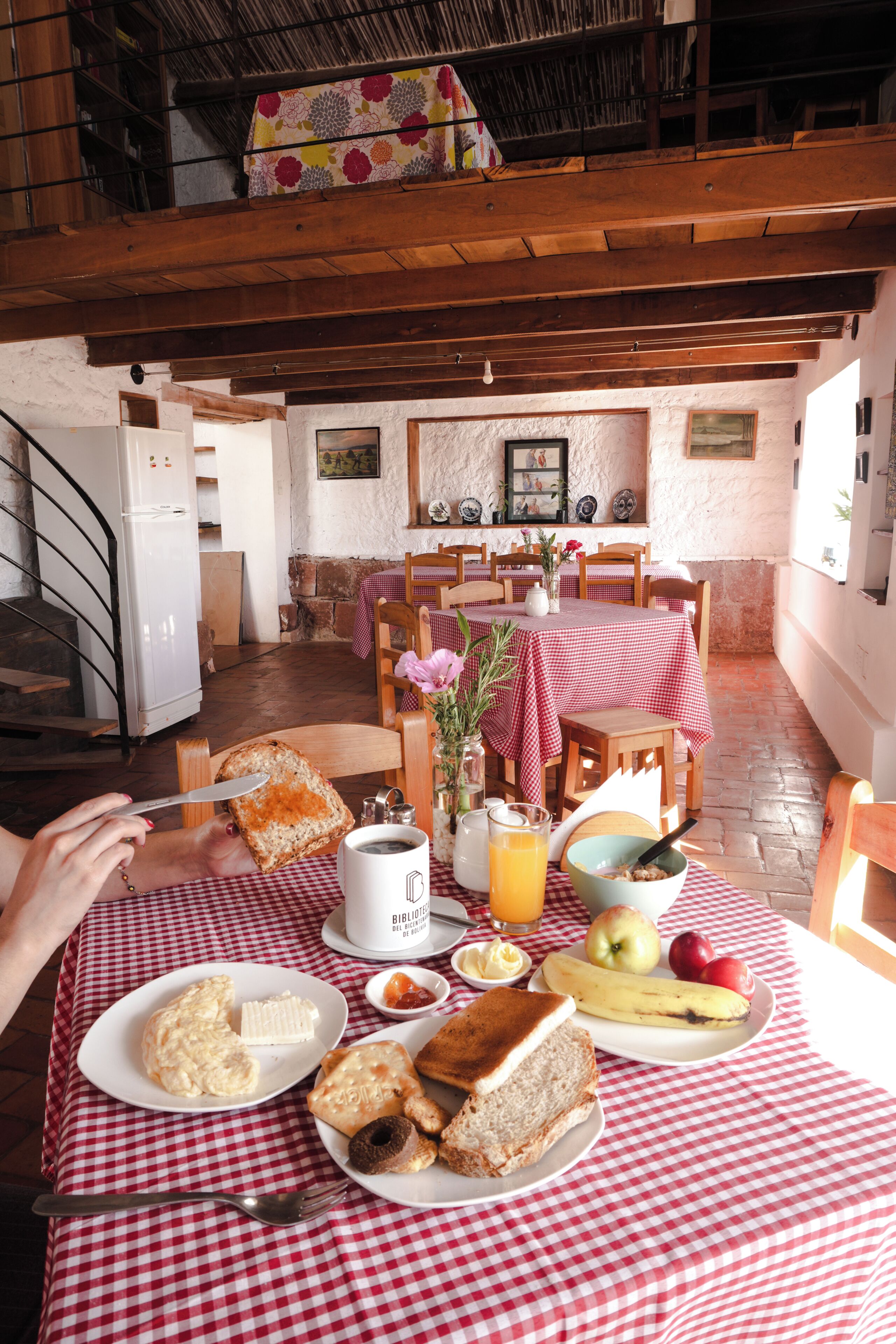 A breakfast setting with a checkered tablecloth, a dining table, chairs, a refrigerator, and a staircase.