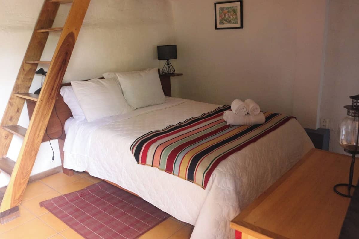 A bed with white linens, a striped blanket, and rolled towels. A wooden ladder is against the wall.