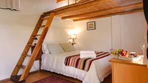 A bedroom with a sloped ceiling, a wooden ladder, a bed with a striped blanket, a nightstand with a lamp, and a fruit plate on the side table. - La Selenita  (Sucre)