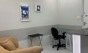A room with a sofa, a small table, a glass-top desk, a black office chair, and two framed artworks on the wall. - Flat Com Vista Mar No Everest (Recife)