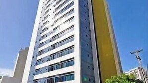 A tall, modern building with multiple floors, large windows, and a distinctive yellow accent on one side. - Flat Com Vista Mar No Everest (Recife)