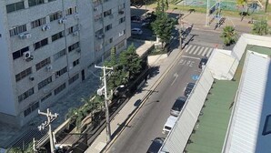 A high-rise building with multiple floors, a street in front, and a beach with palm trees in the background. - Flat Com Vista Mar No Everest (Recife)