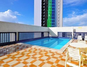 A rooftop swimming pool with a checkered floor, surrounded by white chairs and tables. - Flat Com Vista Mar No Everest (Recife)