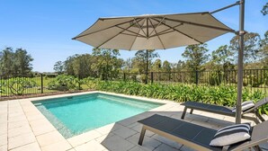 Ein Pool mit Liegebereich, eine Pergola mit Dach und ein angelegter Garten.