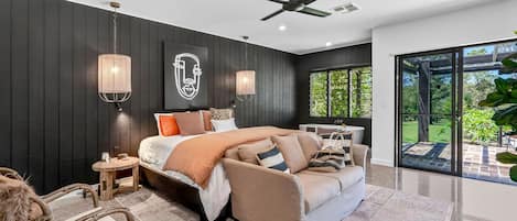 A modern bedroom with a large bed, a sofa, a small table, and a ceiling fan.