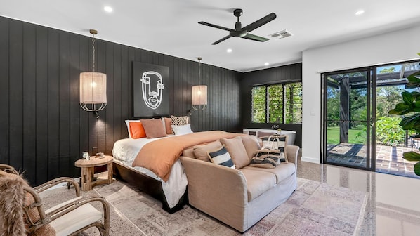 Une chambre moderne avec un grand lit, un canapé, une petite table et un ventilateur de plafond.