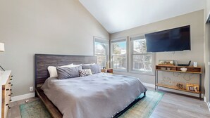 Une chambre avec un grand lit, un téléviseur fixé au mur et une fenêtre donnant sur l’extérieur.