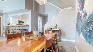 Un grand espace à manger avec une table et des chaises en bois, une cuisine à l’arrière-plan et un escalier menant à un niveau supérieur.