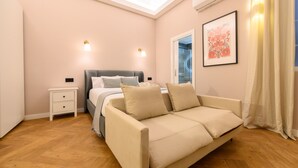 Ein Schlafzimmer mit Bett, Sofa, Nachttisch, Wand-Klimaanlage und einem Fenster mit Vorhängen.