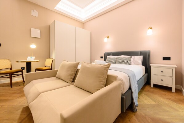 A bedroom with a bed, a sofa, a nightstand, and a desk with a lamp. - M Nda11bid Estudio Interior en el Centro de Madr (Madrid)