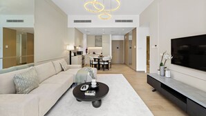 Ein modernes Wohnzimmer mit einer Couch, einem Couchtisch und einem Fernseher. Im Hintergrund ist ein Essbereich mit Tisch und Stühlen zu sehen.