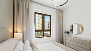 Ein modernes Hotelzimmer mit einem großen Bett, einem Nachttisch, einem Schminktisch, einem runden Spiegel und einem Fenster mit Vorhängen.