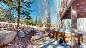 Une cabane en bois avec un jacuzzi, entourée d’une forêt et de grands rochers.