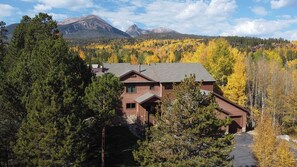 Un chalet à deux étages, doté de fondations en pierre et d’un toit en pente, entouré d’une forêt dense et d’un feuillage automnal.