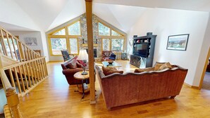 Ein geräumiges Wohnzimmer mit hohen Decken, Holzböden und großen Fenstern mit Blick ins Freie.