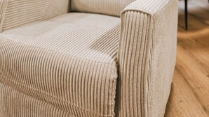 Een beige fauteuil met ribbeltextuur in een moderne keuken met witte kasten en een houten vloer.