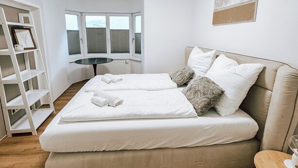 Een slaapkamer met een bed, een nachtkastje, een raam, een radiator en een plank met ingelijste foto's.
