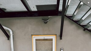 Een gesloten metalen deur met daarboven het getal '3', een metalen ventilatie rooster en een deurmat op de grond.
