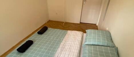 Habitació petita amb un llit individual, un sòl de fusta en rellevat, una porta blanca i un penjador amb ganyots.