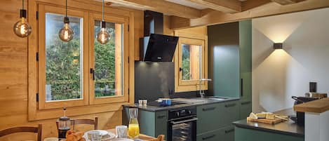 Una cocina moderna con vigas de madera, horno empotrado y comedor con mesa lista para el desayuno.