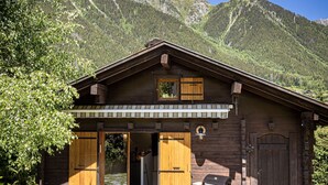 A wooden cabin with a covered patio, a grill, and a mountain backdrop. - Chalet Juno -  sleeps 5 guests, parking, wifi - Chamonix All Year (Chamonix)
