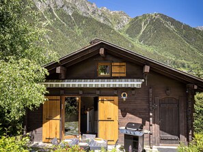 A wooden cabin with a covered patio, a grill, and a mountain backdrop. - Chalet Juno -  sleeps 5 guests, parking, wifi - Chamonix All Year (Chamonix)