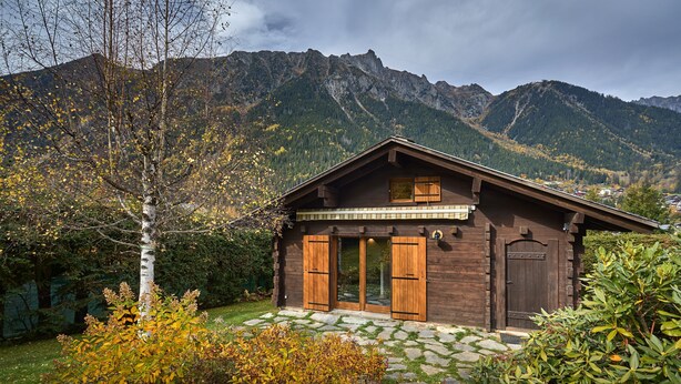A wooden cabin with a stone-paved entrance, surrounded by autumn foliage and mountains in the background. - Chalet Juno -  sleeps 5 guests, parking, wifi - Chamonix All Year (Chamonix)