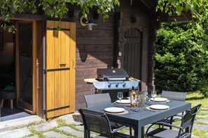 An outdoor dining area with a table set for two, a grill, and a wooden door. - Chalet Juno - Ski, Hike, Bike - Chamonix All Year (Chamonix)