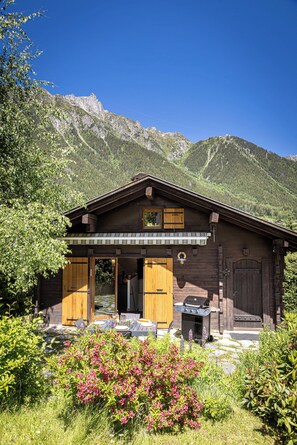 A wooden cabin with a covered patio, surrounded by lush greenery and mountains. - Chalet Juno - Ski, Hike, Bike - Chamonix All Year (Chamonix)