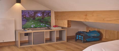 Un dormitorio con una televisión sobre un soporte de madera, una cama, una maleta y una mesita de noche con un libro.