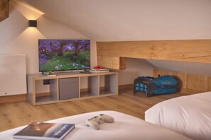 A bedroom with a TV on a wooden stand, a bed, a suitcase, and a small table with a book. - Chalet Juno - Ski, Hike, Bike - Chamonix All Year (Chamonix)