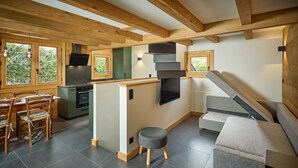 A modern kitchen with wooden beams, a dining area with a table and chairs, a grey sofa, and a small ottoman. - Chalet Juno -  sleeps 5 guests, parking, wifi - Chamonix All Year (Chamonix)