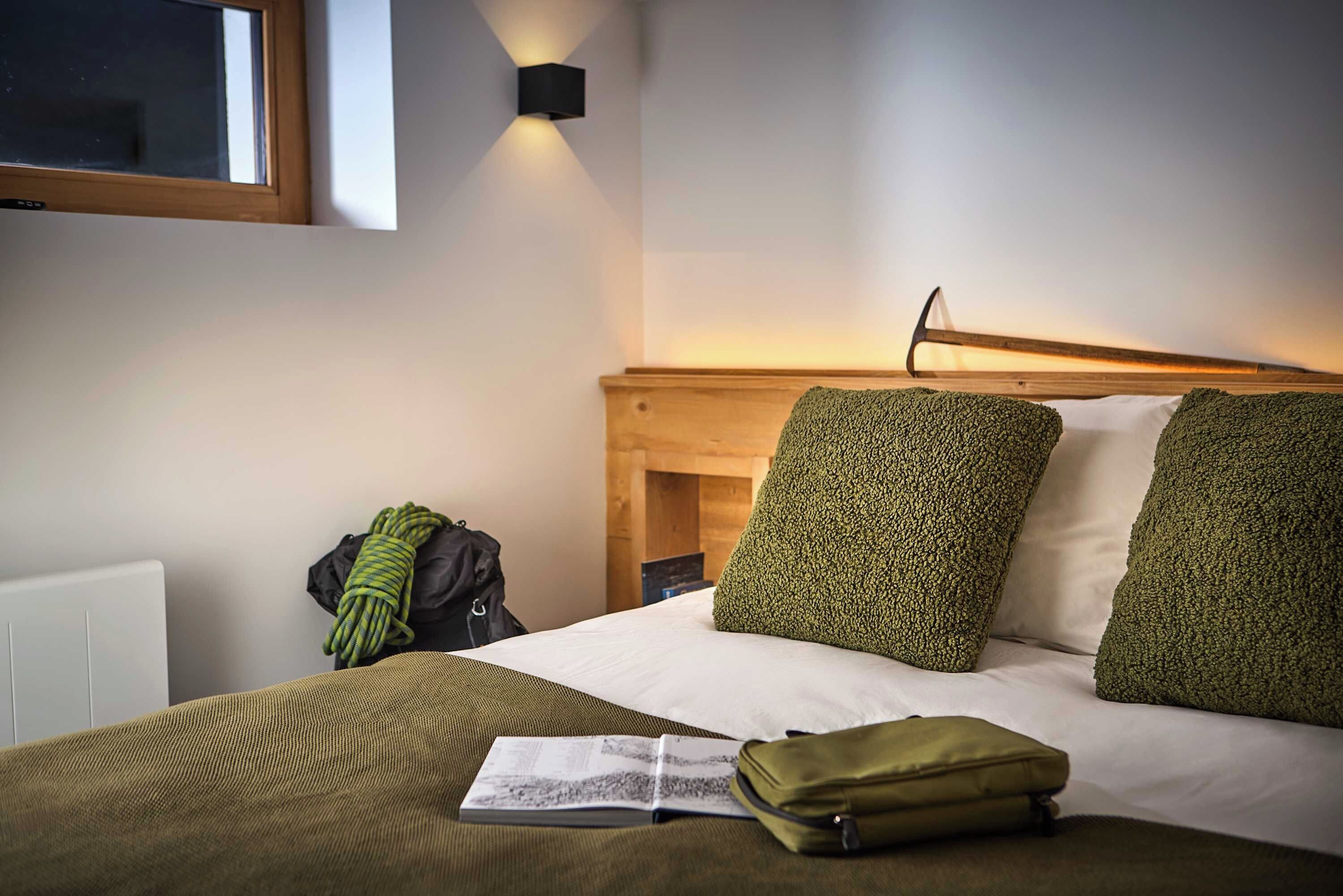 A hotel room with a bed, a reading book, a green bag, and a wall-mounted light fixture.