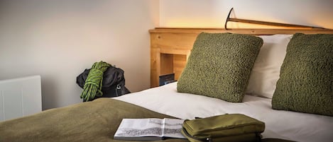 Una habitación de hotel con una cama, un libro para leer, un bolso verde y una lámpara de pared.