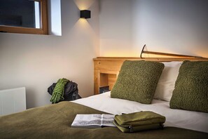 A hotel room with a bed, a reading book, a green bag, and a wall-mounted light fixture. - Chalet Juno - Ski, Hike, Bike - Chamonix All Year (Chamonix)