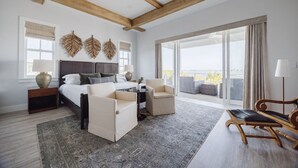 Quarto moderno com uma cama grande, um espaço de estar com uma poltrona, uma mesinha e uma varanda com vista.