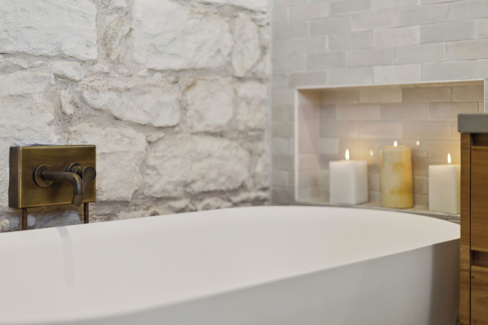 A modern bathroom with a freestanding bathtub, stone wall, and candles.