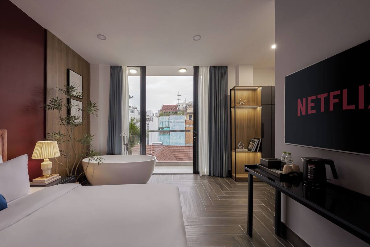 A modern hotel room with a large bed, a bathtub, a TV, and a view of the cityscape.