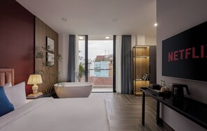 A modern hotel room with a large bed, a bathtub, a TV, and a view of the cityscape. - Lovera Hotel Airport (Ho Chi Minh City)