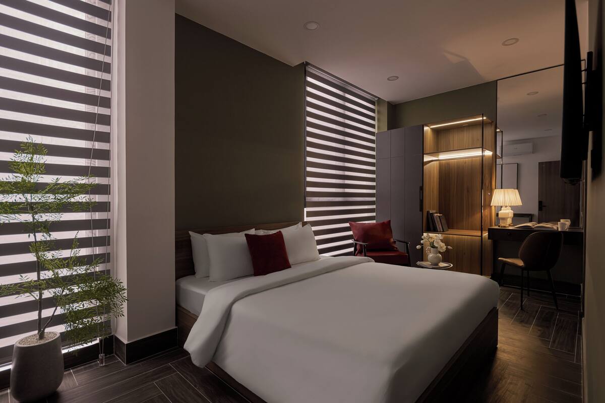 A modern hotel room with a large bed, a desk, a chair, and a potted plant.