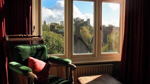 A room with a view of a castle through a large window, a green armchair, and a small wooden table. - Lewes Sauna House · Characterful Interiors, Castle Views (East Sussex)