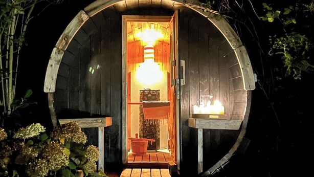 A wooden cabin with a circular entrance, a small porch, and a lit interior. - Lewes Sauna House · Characterful Interiors, Castle Views (East Sussex)