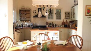 A kitchen with a wooden table, chairs, a potted plant, and various kitchen items. - Lewes Sauna House · Characterful Interiors, Castle Views (East Sussex)