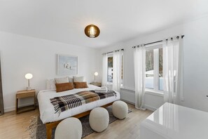 Een slaapkamer met een groot bed, bedlampen, een schilderij en uitzicht op een besneeerd landschap door het raam.