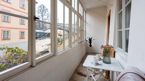 A balcony with large windows, a small table with a vase of flowers, and a view of a building across the street. - Charming Riverside Apartment near Charles Bridge by EasyBNB Premium (Prague)