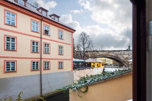 A building with multiple windows, a stone bridge in the background, and a snow-covered area. - Charming Riverside Apartment near Charles Bridge by EasyBNB Premium (Prague)