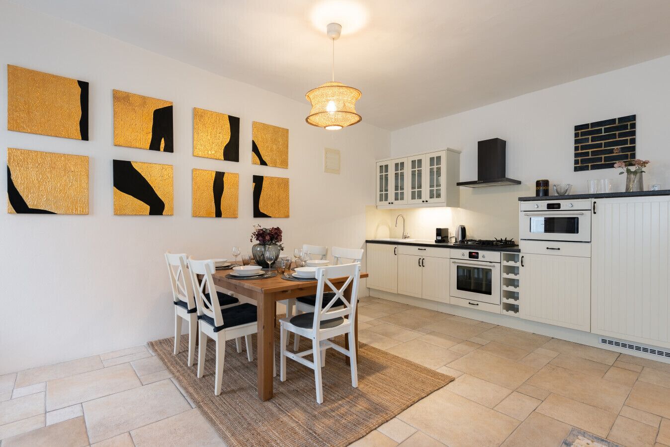 Une cuisine moderne avec des meubles blancs, une table à manger avec des chaises et des œuvres d’art abstraites aux couleurs or et noir accrochées au mur.